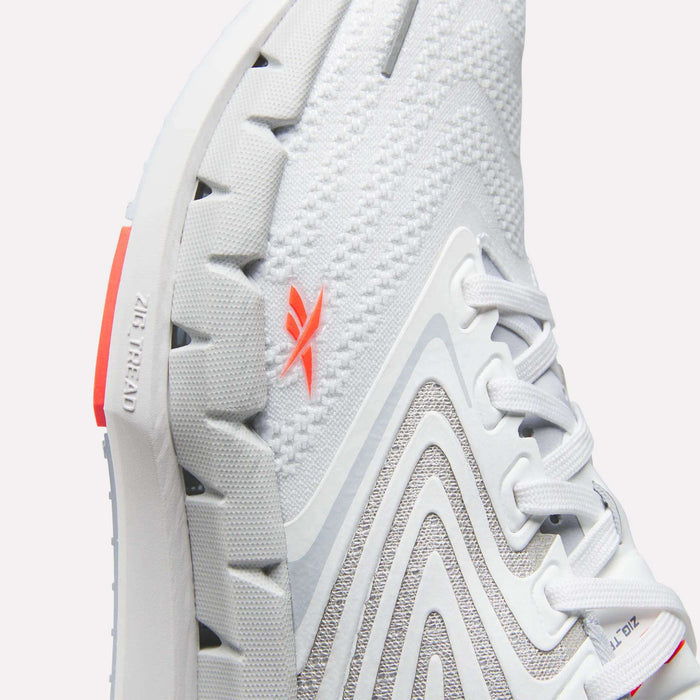 Close-up of Reebok Women's FloatZig Tread Running Shoe with breathable mesh, textured sole, gray curved patterns, white laces, and an orange logo. “Zig Kinetica” and “Zig” are embossed near the heel on the sole.