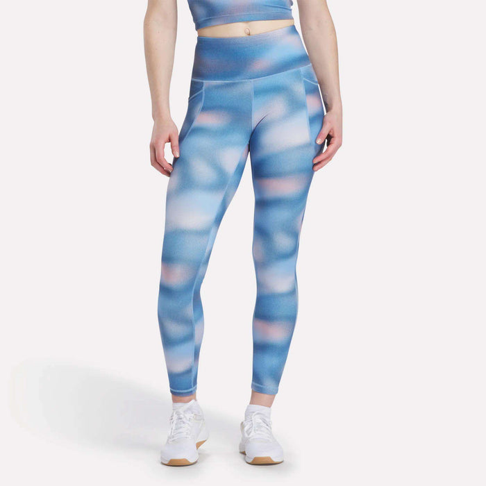 Person wearing Reebok Women's Fluid Print High-Rise Tights with a matching crop top, shown from the shoulders down, arms relaxed at their sides, paired with white sneakers.