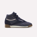 A pair of Reebok Women’s Freestyle Hi Shoes in Darkindigo/Chalk/Gum—a classic high-top silhouette featuring two velcro straps, a white midsole, a brown gum outsole, and pink accents—displayed against a plain light background.
