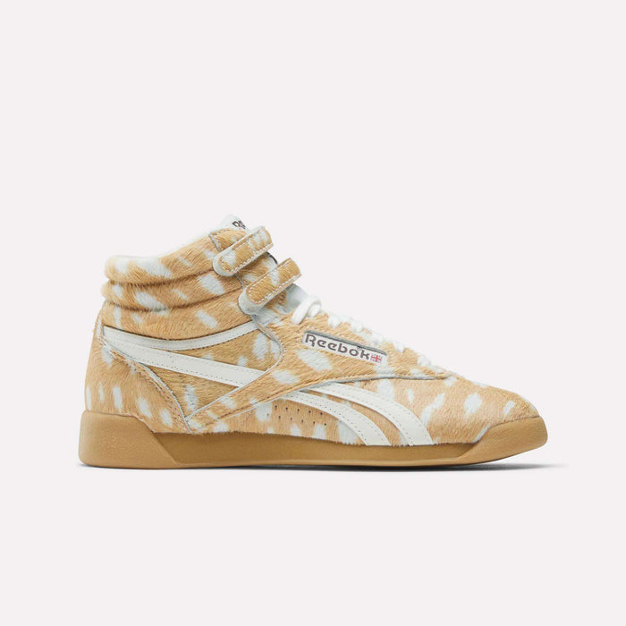 The Reebok Women's Freestyle Hi Shoes are high-tops inspired by 80s fitness, featuring tan and white deer-patterned fur, signature white stripes, a gum sole, and velcro straps above the laces.