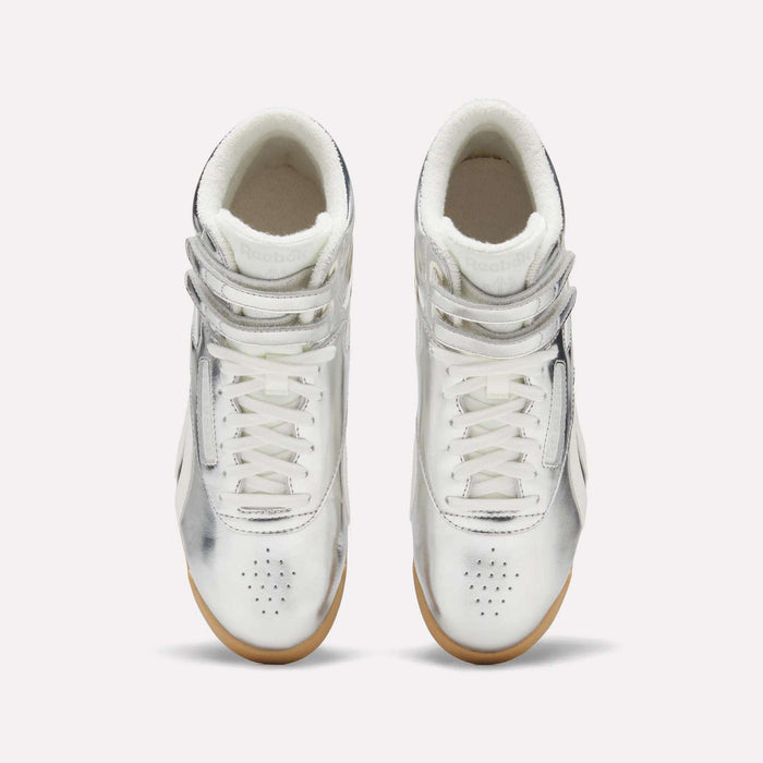 A pair of Women’s Freestyle Hi Shoes by Reebok in high-top, metallic silver premium leather, featuring Velcro straps and white laces, displayed from above on a plain light background.