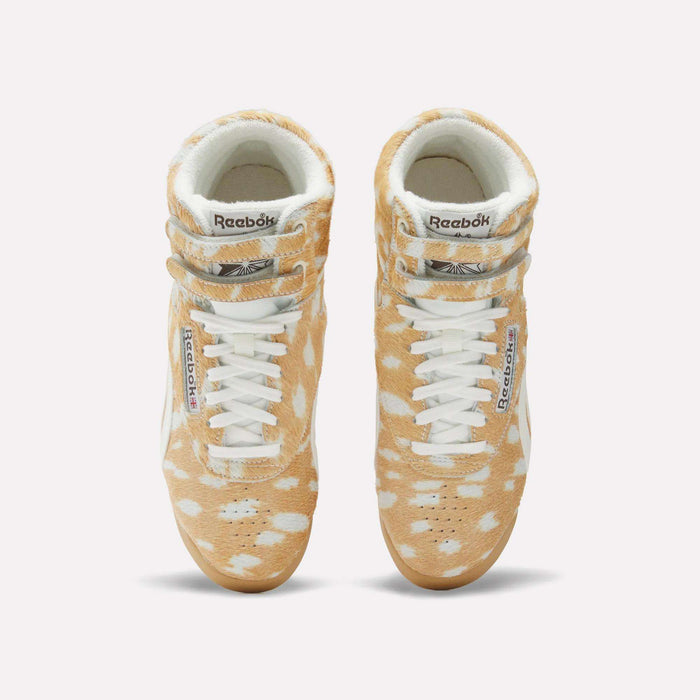 Top view of Women's Freestyle Hi Shoes by Reebok, featuring a classic 80s high-top design with a tan and white spotted fur-like pattern, white laces, and signature Reebok branding on the tongue and side.