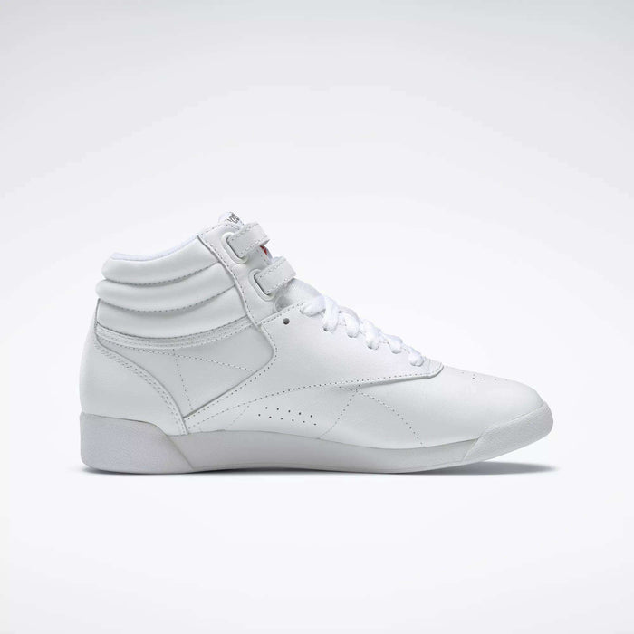 The Reebok Women's Freestyle Hi Shoes are white high-top sneakers with laces and velcro straps, showcasing a minimalist design and subtle stitching—perfect for women's fitness routines. Shown in a side view on a plain light background.