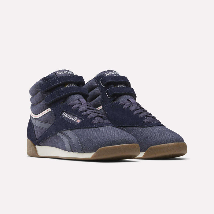A pair of Women’s Freestyle Hi Shoes by Reebok in navy blue, featuring high-top design with velcro straps, suede and leather accents, white midsoles, and gum rubber outsoles, showcased against a plain white background for a classic Reebok appearance.