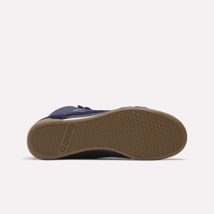 The Reebok Women’s Freestyle Hi Shoes are displayed from the sole, showcasing a navy blue upper with a light brown rubber outsole featuring a textured hexagonal pattern and Reebok branding near the heel.