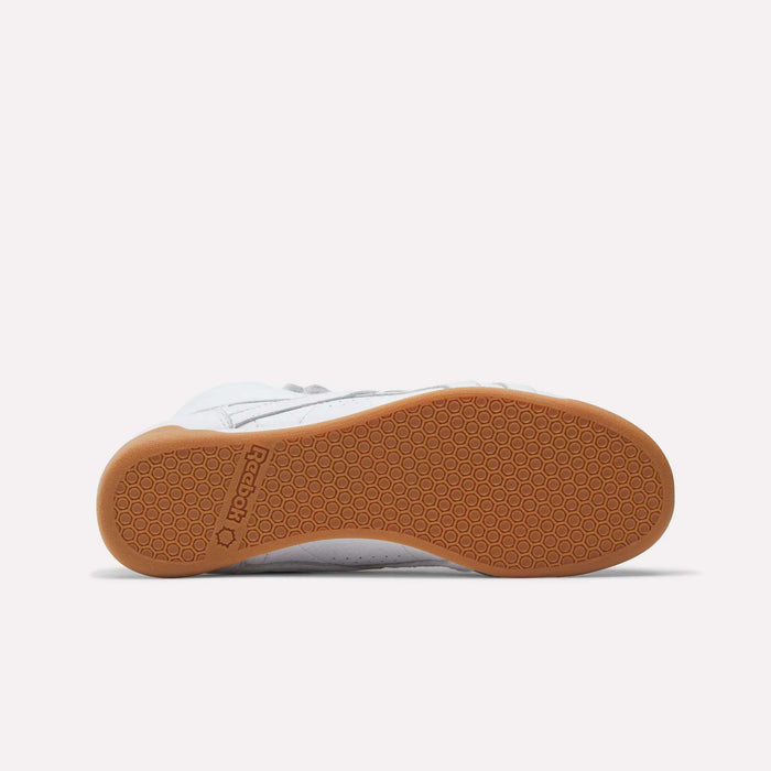 The Reebok Women's Freestyle Hi Shoes are shown from the bottom, showcasing a white upper, light brown gum sole with a hexagonal tread pattern, and the Reebok logo near the heel—a tribute to 80s fitness classics.