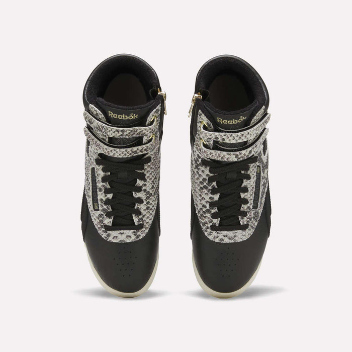 Top view of a pair of Reebok Women’s Freestyle Hi Zip Shoes in black, featuring white soles, black laces, and snakeskin-patterned accents on the straps and upper sides, displayed against a plain white background. These Reebok sneakers showcase an iconic retro women’s leather style with bold detailing for a standout look.