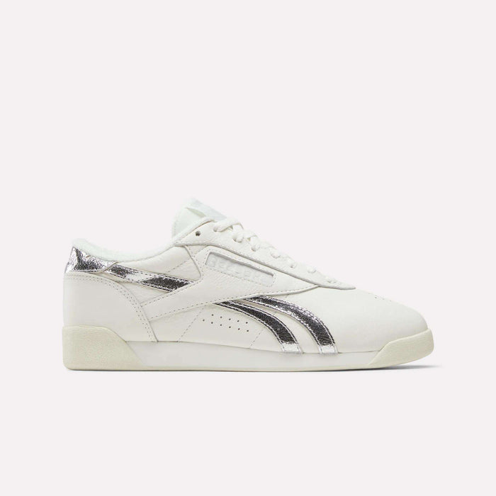 The Reebok Women's Freestyle Lo Shoes in Chalk/Silvermetallic/Vintagechalk feature a low-profile side view with silver metallic accents on the logo and heel, set against a plain light background.