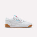The Women's Freestyle Lo Shoes by Reebok are shown in side profile on a plain white background, featuring white leather, a gum sole, blue Reebok branding, and red and blue accents.
