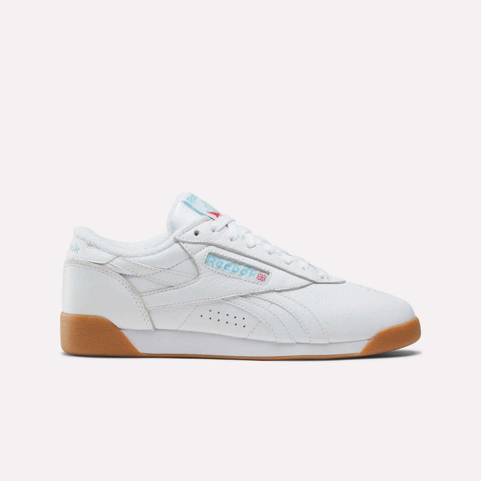 The Women's Freestyle Lo Shoes by Reebok are shown in side profile on a plain white background, featuring white leather, a gum sole, blue Reebok branding, and red and blue accents.