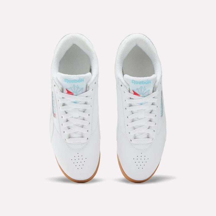 Top view of Reebok Women's Freestyle Lo Shoes in white with white laces, light blue branding on the tongue, perforated toe area, and light brown gum soles, set against a plain white background.