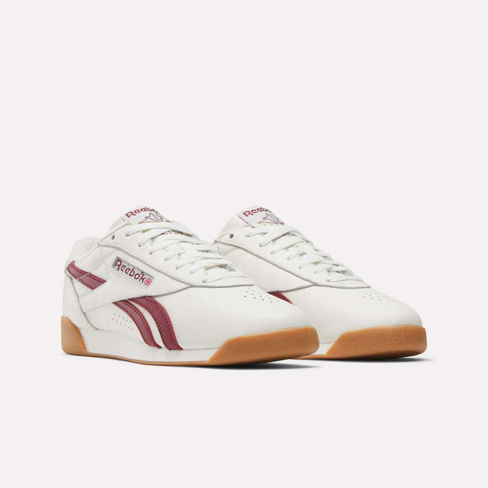 The Women's Freestyle Lo Shoes by Reebok are retro white sneakers with maroon stripes and logo, gum-colored soles, shown against a plain white background.