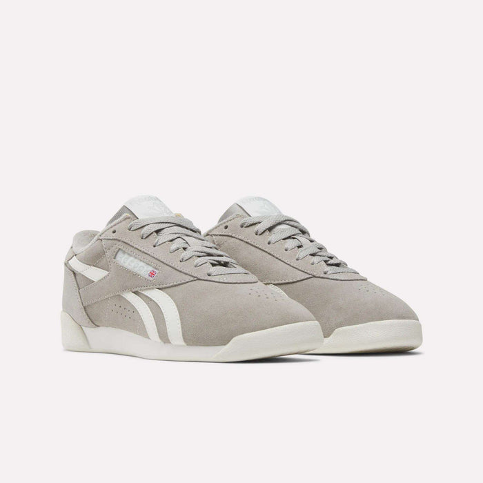 The Reebok Women's Freestyle Lo Shoes are retro sneakers in light gray suede with white soles and side stripes, shown on a simple light background.