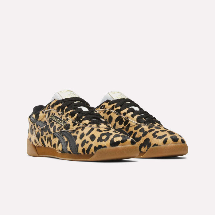 The Reebok Women's Freestyle Lo Shoes feature a tan and black leopard print pony hair upper, black laces, and brown rubber soles, shown against a plain white background.