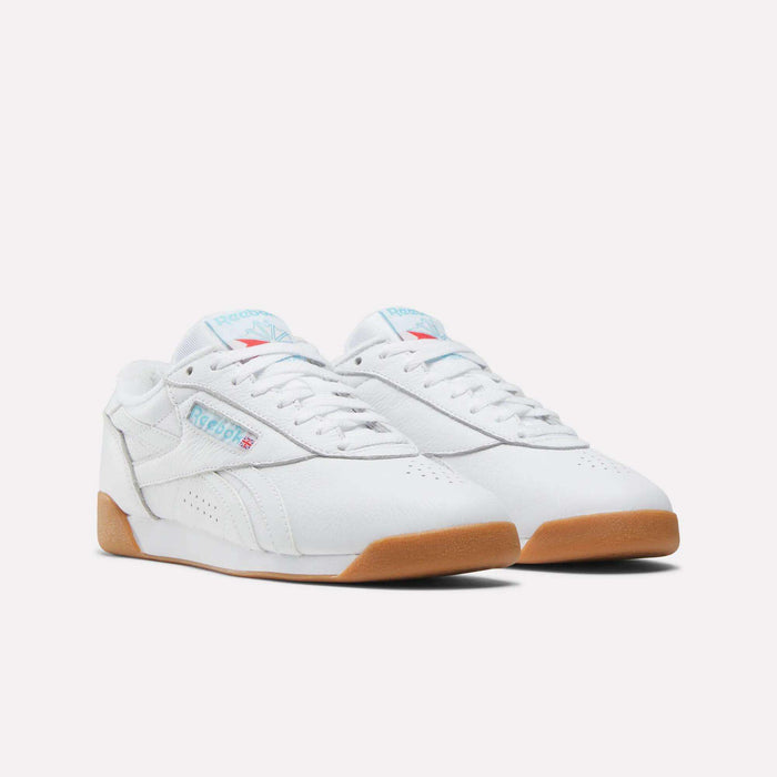 The Women's Freestyle Lo Shoes by Reebok feature white leather with light blue accents, classic logo detailing, and tan gum rubber soles, displayed on a plain white background.