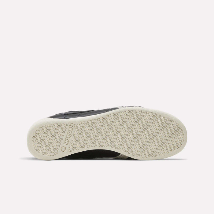 The image displays the sole of the Reebok Women’s Freestyle Lo Shoes in black, featuring a white, textured rubber outsole with a distinctive honeycomb pattern and an embossed Reebok logo near the heel. This classic style captures the signature quality and design of these women’s sneakers from Reebok.