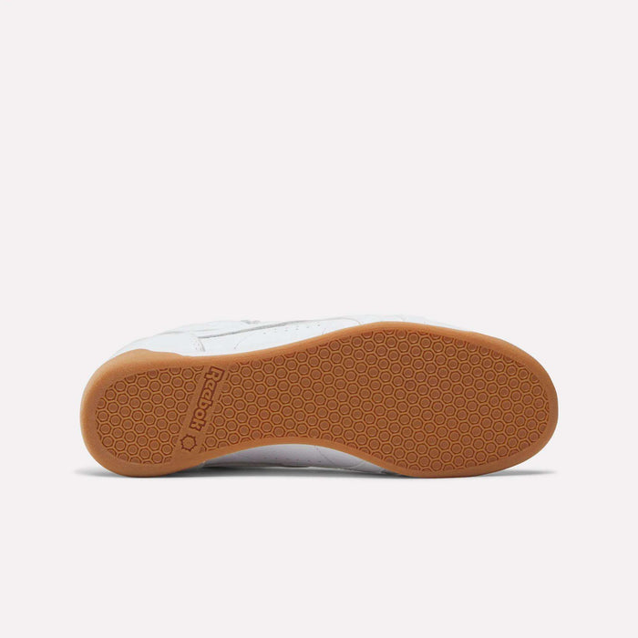 The Reebok Women's Freestyle Lo Shoes feature white leather uppers and a textured light brown rubber sole with a honeycomb pattern, plus the Reebok logo by the heel—an iconic choice in women’s footwear.