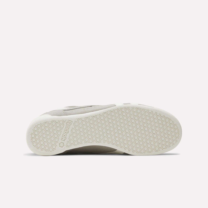 A Women's Freestyle Lo Shoe by Reebok lies on its side, highlighting the textured, hexagon-patterned rubber sole with a Reebok logo near the heel. This retro sneaker stands out against a plain white background.