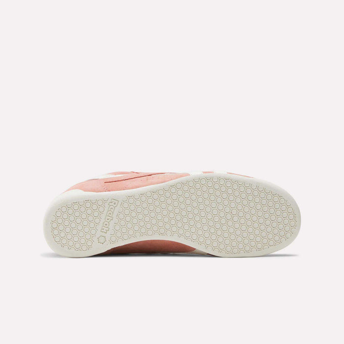 The Reebok Women's Freestyle Lo Shoes in pink and white feature a retro sneaker design, shown from the side to highlight the textured white rubber sole with a hexagonal pattern.