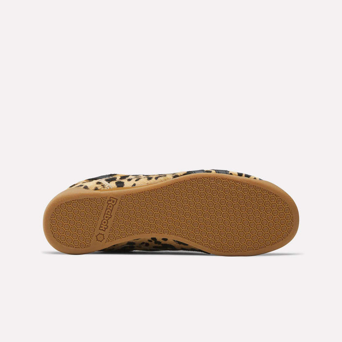 The image displays the sole of the Reebok Women's Freestyle Lo Shoes with a tan rubber hexagonal tread, leopard print sides in tan and black, and a pony hair upper inspired by '80s fitness trainer style.
