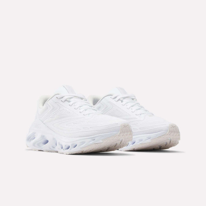 The Reebok Women's Fuel Flex Run Shoes in white feature textured soles and wavy Fuel Flex midsoles, shown against a light background.