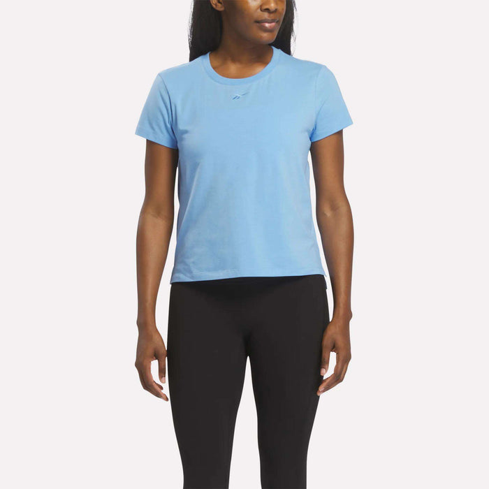 A woman wearing a Vector Peri Blue Reebok Women's Graphic Glow Top and black leggings stands facing forward against a plain white background.