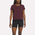 A woman wearing a Reebok Women's Graphic Glow Top in Wine Tasting and black fitted shorts stands against a plain white background.
