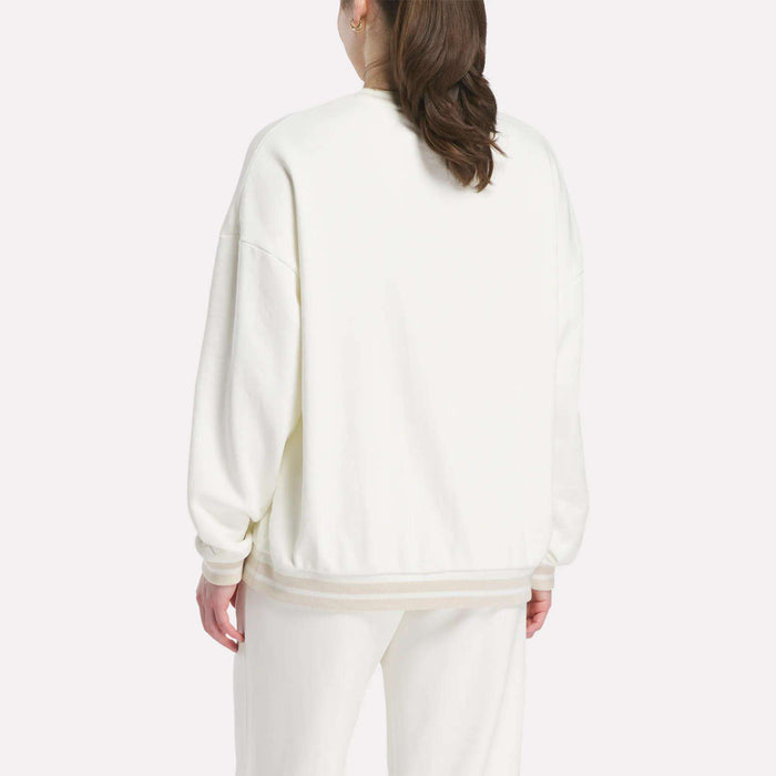 A woman with long brown hair is seen from the back against a plain light background, wearing Reebok's Women's Lawn Club Crew Sweatshirt in white with matching pants.