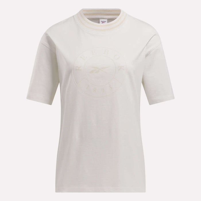 The Reebok Women's Lawn Club T-Shirt is a plain white tee with short sleeves and a ribbed crew neck. It features an embossed Reebok logo and text on the front, shown against a light background.