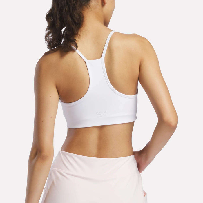 A woman is seen from the back in a Reebok Women's Low-Impact Sports Bra with adjustable straps and light pink leggings, standing against a plain background.