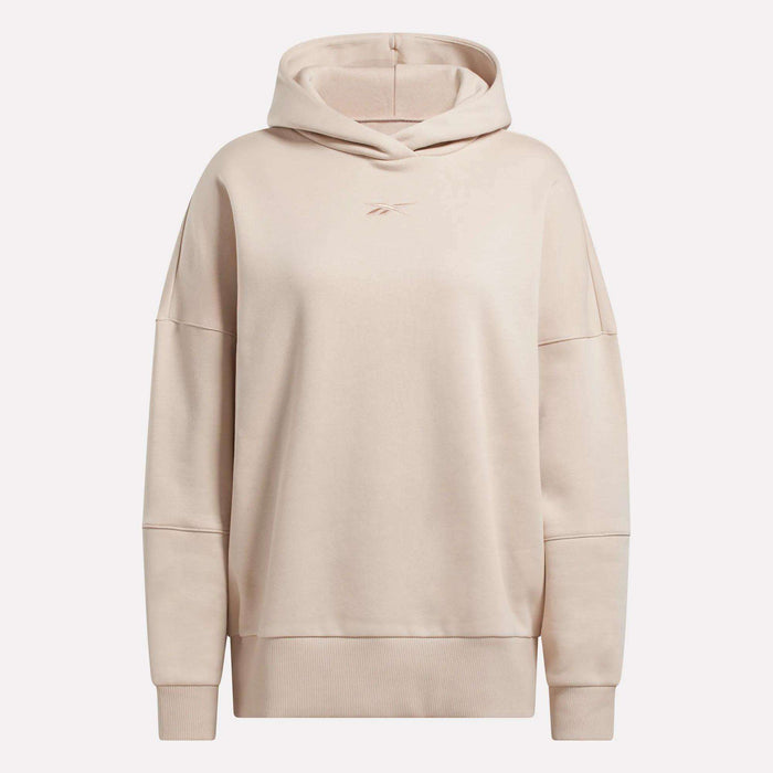 The Women's Lux Hoodie by Reebok features a beige, oversized design with long sleeves, a relaxed fit, and a small embroidered Reebok logo on the chest. This cozy hoodie is shown against a plain white background.