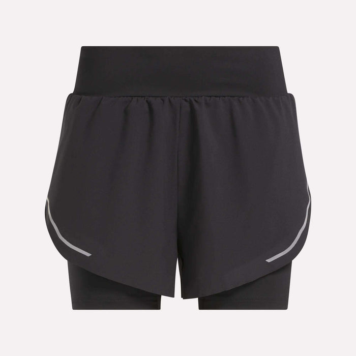 The Reebok Women's Lux Metallic 2-in-1 Running Shorts 3" are black, high-waisted shorts with an overlapping front layer, reflective curved side stripes, and fitted inner shorts. Shown against a plain light gray background.