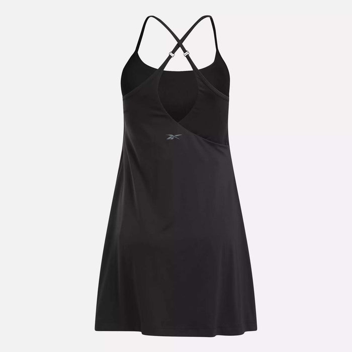 The Reebok Women's Lux Strappy Dress features thin crisscross back straps, a fitted bodice, flared skirt, and front logo. Made from moisture-wicking fabric to keep you cool. Displayed on a plain white background.
