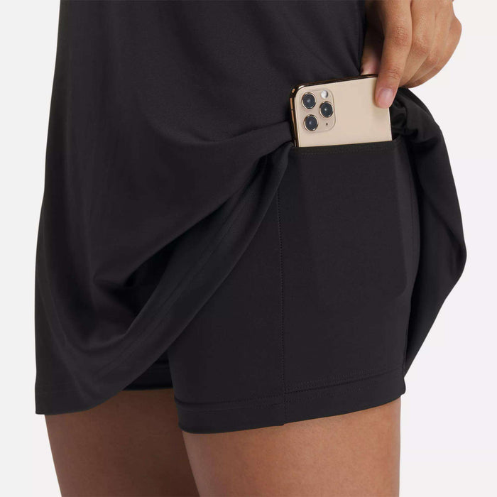 A person slips a smartphone into the side pocket of Reebok’s Women's Lux Strappy Dress, lifting the black top layer slightly as they do.