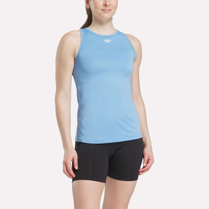 A woman wears a Reebok Women's Marled Performance Tank Top in light blue with black shorts, standing against a plain white background.