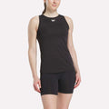 A woman wearing the Reebok Women's Marled Performance Tank Top stands with one arm relaxed by her side, smiling slightly against a plain white background.