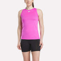 A woman wears a sleeveless bright pink Reebok Women's Marled Performance Tank Top and black shorts, standing against a plain white background.