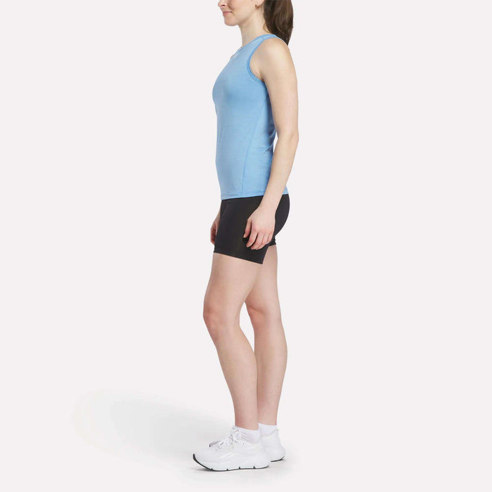 A person stands in profile facing right, wearing a light blue Reebok Women's Marled Performance Tank Top, black shorts, white socks, and white athletic shoes against a plain white background.