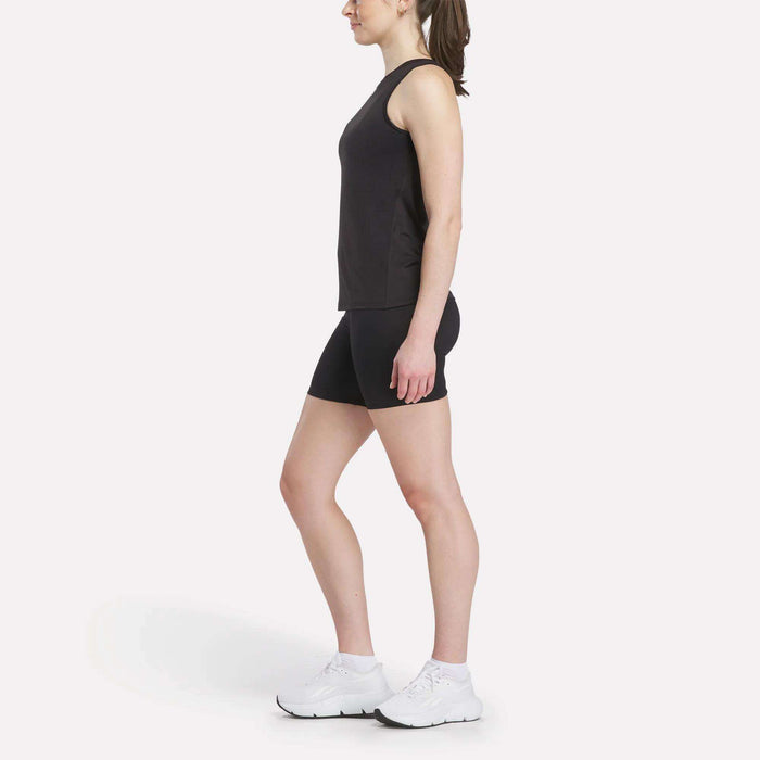 A woman in profile faces left, wearing a Reebok Women's Marled Performance Tank Top and black shorts with white athletic shoes—ideal activewear—set against a plain white background.