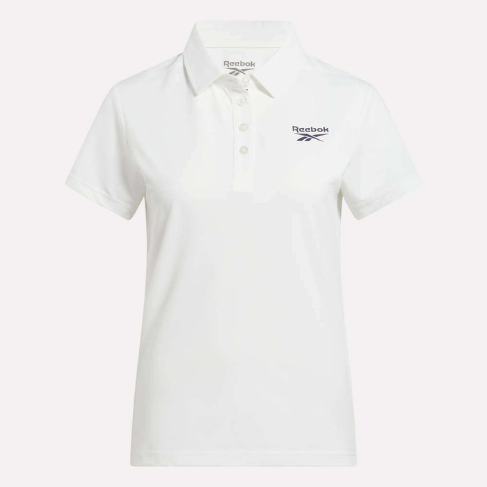 The Reebok Women's Micro Pique Polo Shirt is a white, short-sleeve collared polo with three buttons and a navy Reebok logo on the left chest. Made from stretch fabric for comfort and easy movement on the golf course.