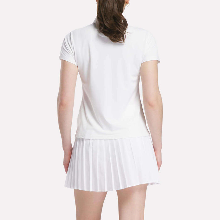A woman is seen from the back wearing a Reebok Women's Micro Pique Polo Shirt with short sleeves and a white pleated skirt, standing against a plain light background.