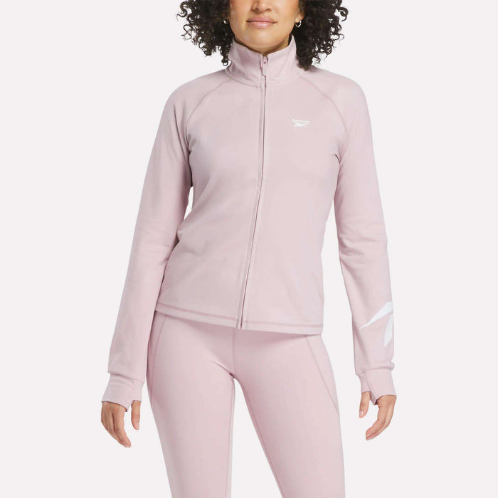 A person wearing a light pink Reebok Women's Motion Core Full-Zip Hoodie and matching leggings, standing with arms relaxed by their sides against a plain white background.