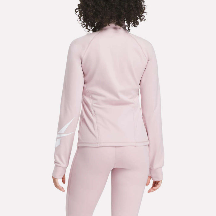 A woman with curly hair is seen from the back wearing the Reebok Women's Motion Core Full-Zip Hoodie in light pink with a white diagonal design on the right sleeve—perfect for workouts. Matching leggings complete her athletic look.