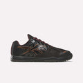 A side view of the Women’s Nano 2.0 Training Shoes by Reebok is shown against a plain white background, highlighting their black and copper colorway, mesh panel detailing, and textured sole—features that showcase the sleek design and functional fitness performance characteristic of Reebok training footwear.