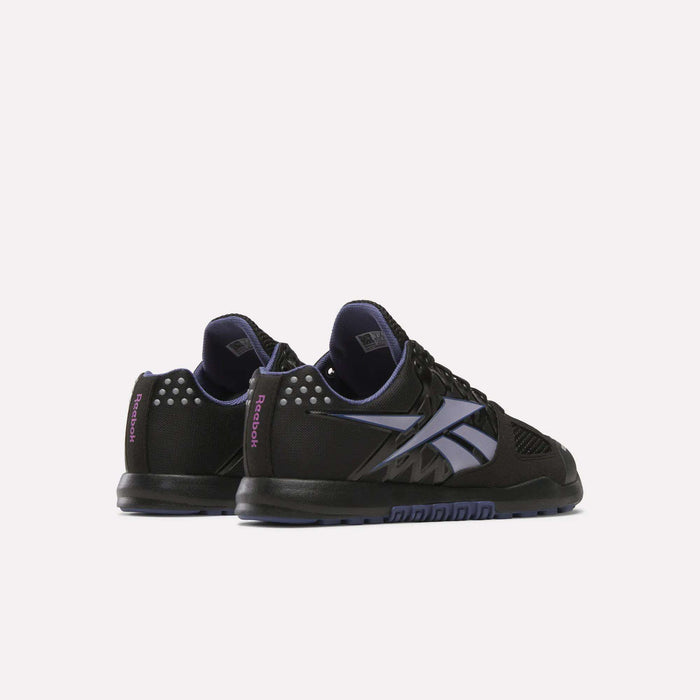 The Women's Nano 2.0 Training Shoes by Reebok are shown in black with purple accents, a large side Reebok logo, and decorative heel studs—ideal for functional fitness, displayed from a rear side angle on a white background.
