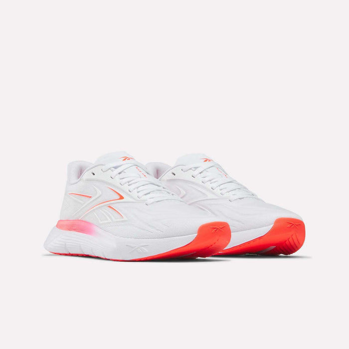 The Women's Nano Gym 2.0 Training Shoes by Reebok feature a low-top, white athletic design with light pink details and orange accents on the midsole and outsole, shown against a plain light background.