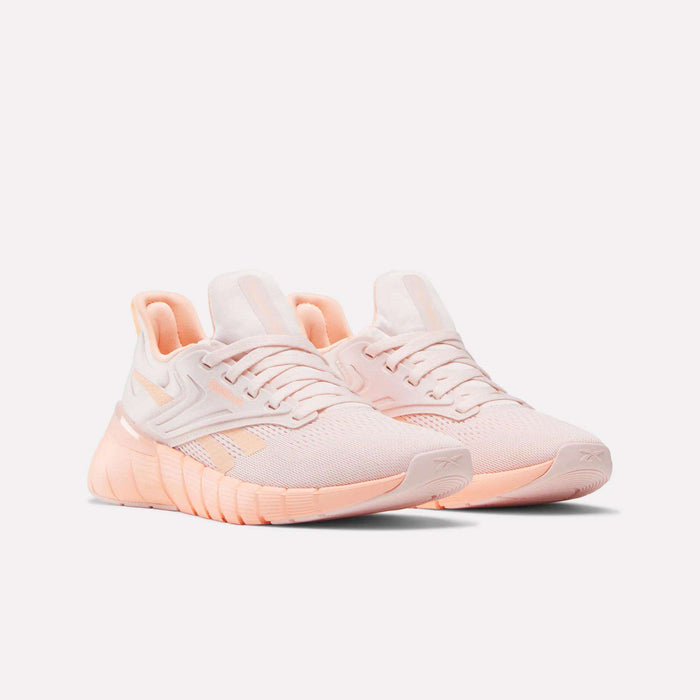 A pair of light pink Reebok Women's Nano Gym Training Shoes with white accents and textured soles are displayed on a light background, facing slightly to the right.