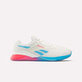 The Women's Nano X4 Training Shoes by Reebok are white with blue and pink accents, a blue Reebok logo, and a gradient pink-to-blue sole. These lightweight shoes are shown on a plain white background.