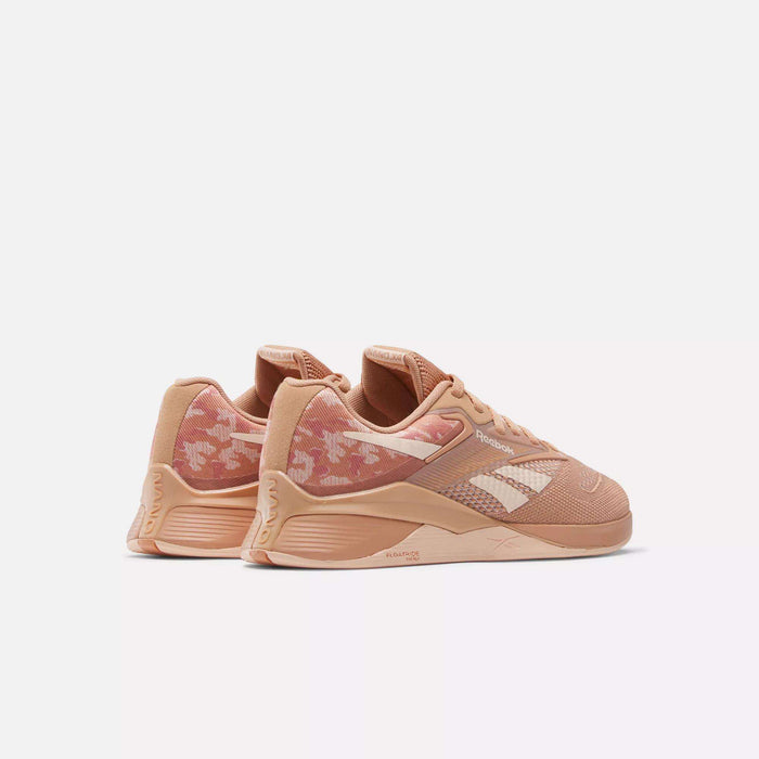 The Reebok Women's Nano X4 Training Shoes feature a peach color with white accents and pink floral heel patterns, offering a lightweight, breathable design. Displayed against a plain white background.