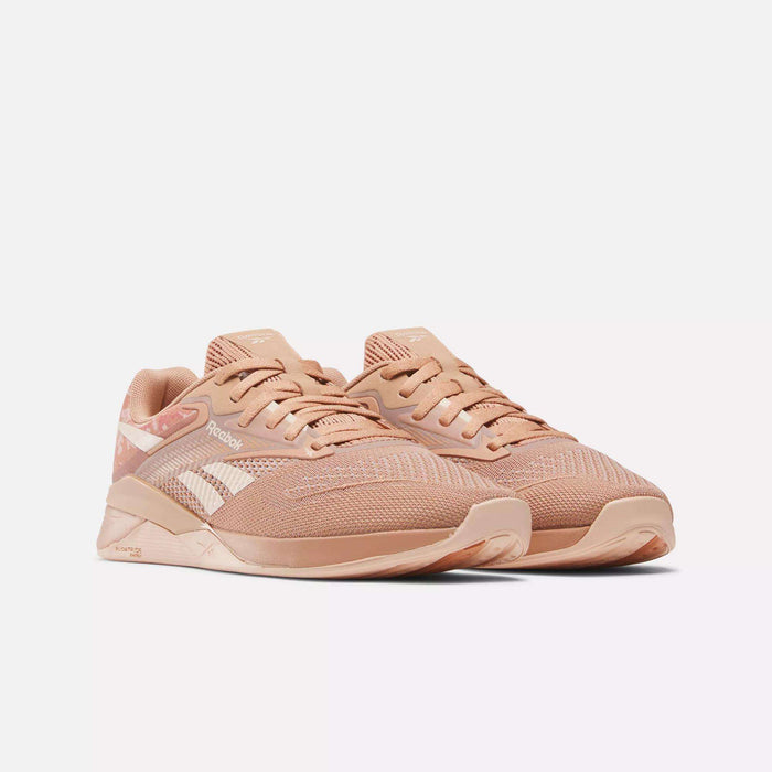 A pair of Reebok Women's Nano X4 Training Shoes in peach with breathable mesh uppers, white side logos, and beige rubber soles are displayed on a plain white background.